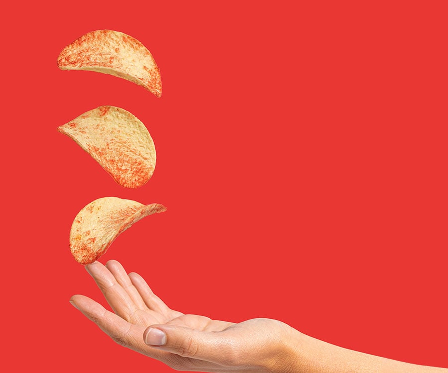 hand and 3 pringles crisps on an orange background